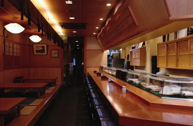 A long counter with a chilled fish display, and opposite it low tatami seating and paper lamps