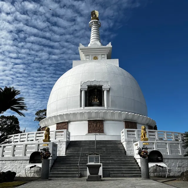 A white dome shaped pagoda with a spire, steps and gilded lion statues