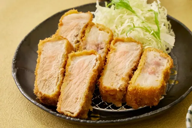 A black plate with slices of crumbed cutlet and a mound of finely shredded cabbage