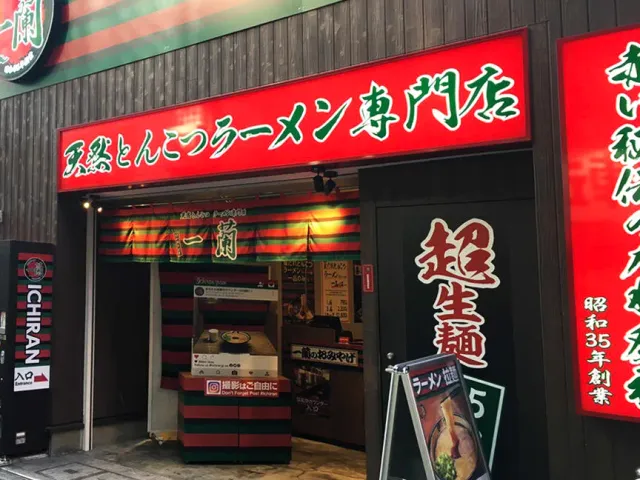 A frontage with a huge red sign, a striped fabric curtain and a ticket machine at the entrance