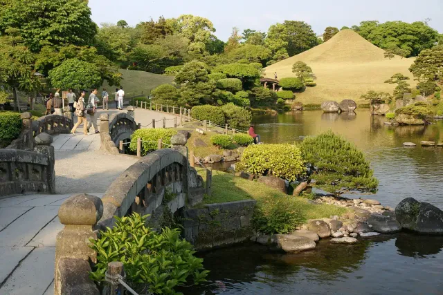 A landscape garden with a conical grass hill, a pond and a stone bridge