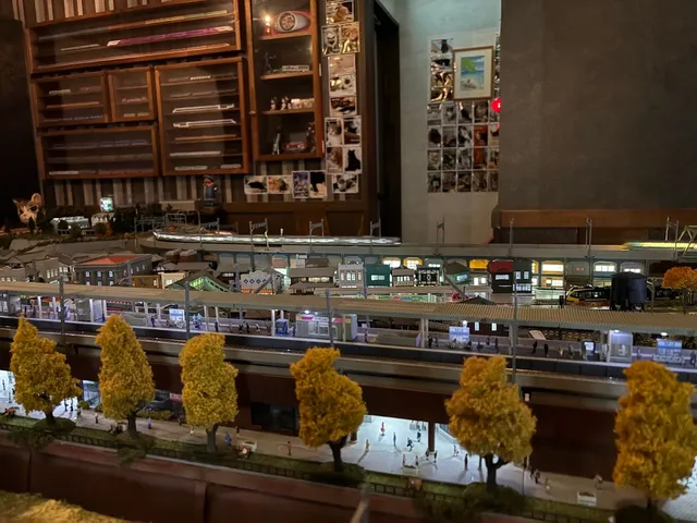 A lit model railway with yellow trees, in front of wooden display cabinets