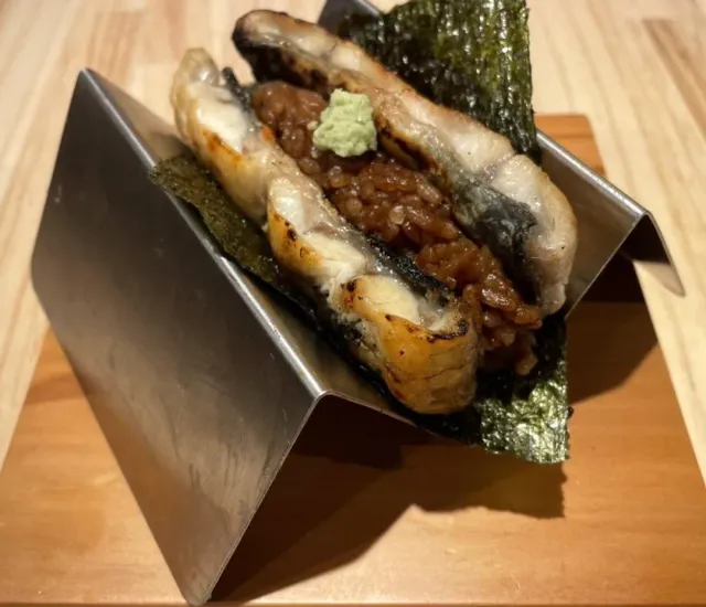 Slices of grilled fish over rice wrapped in seaweed in a metal holder, with wasabi