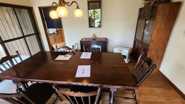 A dining room with a dark wooden table, high backed chairs, a sideboard and a three bulb chandelier