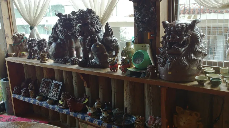 Wooden shelves loaded with dark clay shisa lion figures and glazed ceramic ware inside a shop