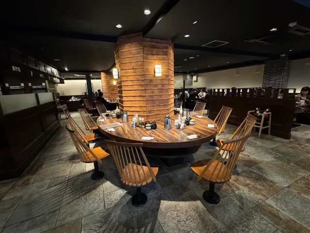 A large round wooden table with chairs around a brick pillar, in a dimly lit hall