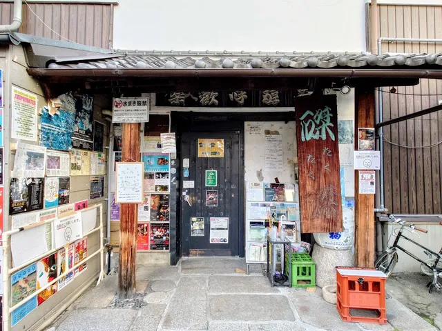 An old entrance with a tiled roof and a dark door, covered in concert posters