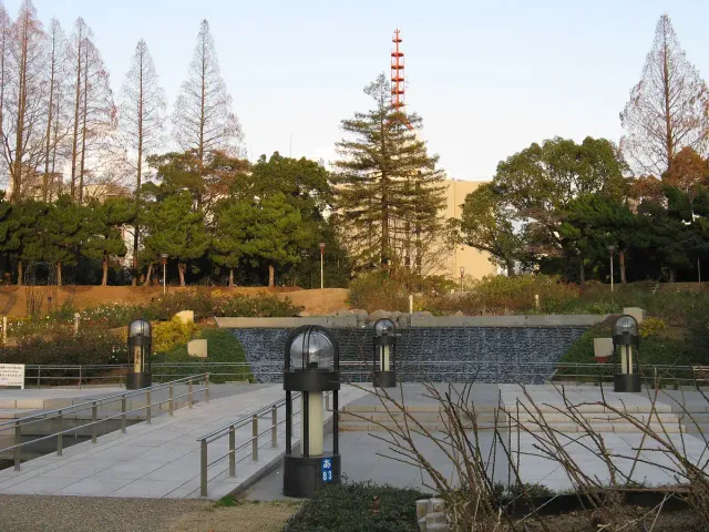 A tree-lined path in a city park with a tower structure behind