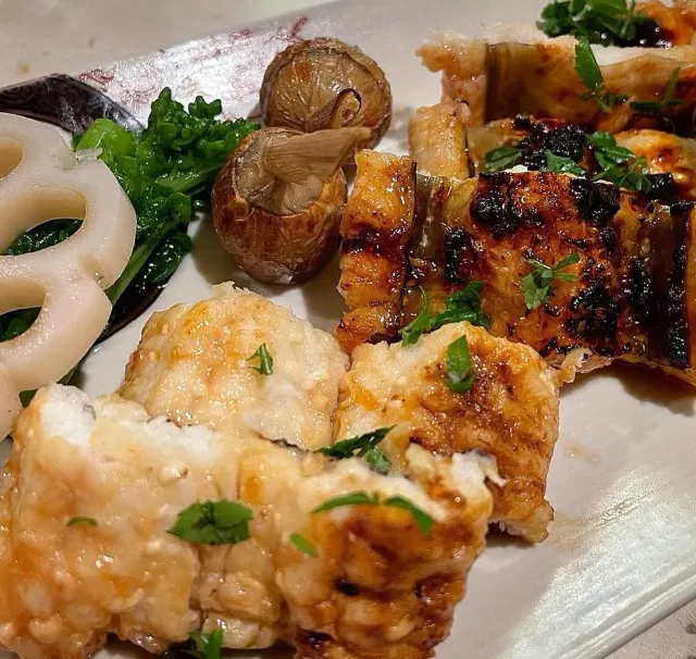 A plate with grilled pieces, whole mushrooms, lotus root slices and green vegetables