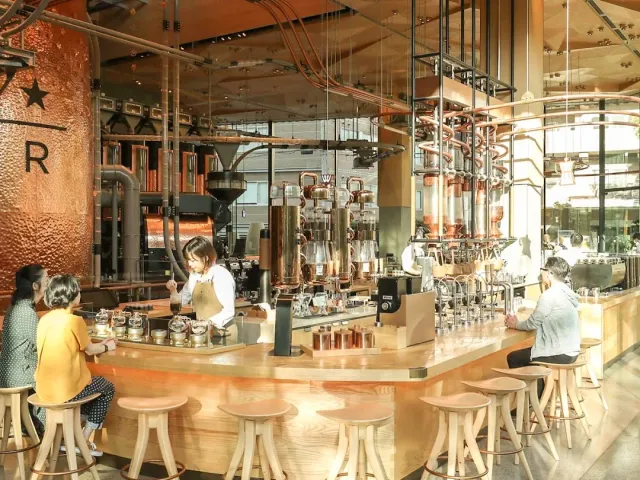 A curved wooden counter facing copper tanks and pipes, with stools and seated customers