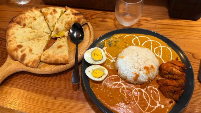 A curry plate with rice, boiled egg and chicken, beside flatbread on a wooden board