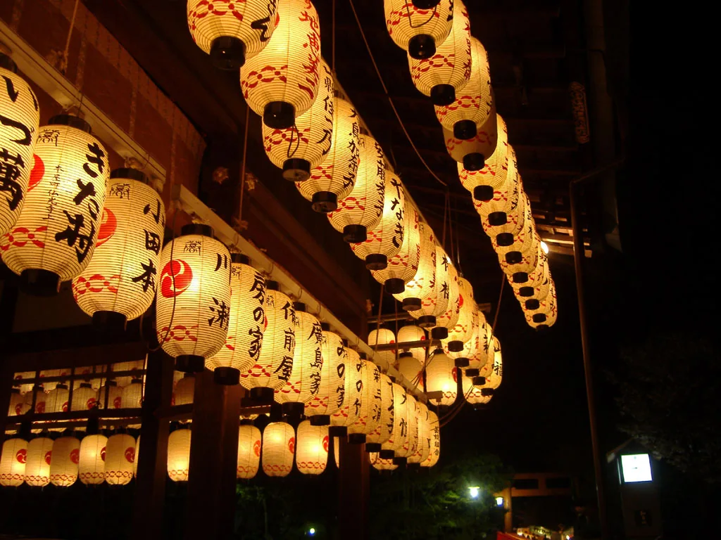 Rows of lit paper lanterns hanging on the dance stage at Yasaka Shrine, each bearing a donor name in Japanese