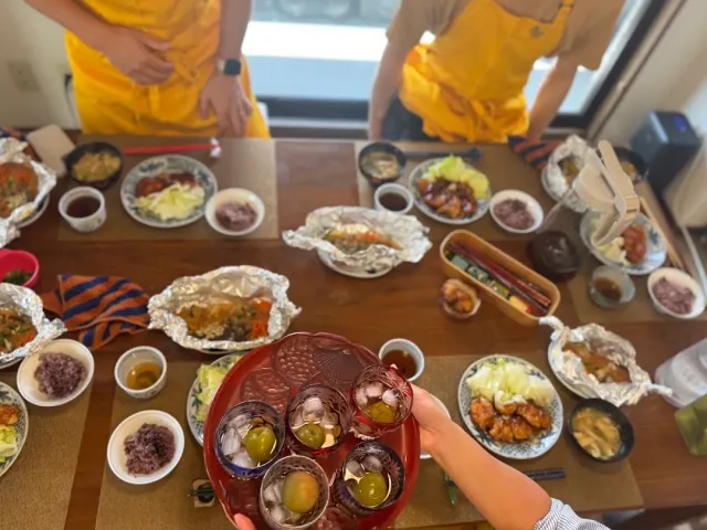 A table laden with home cooked dishes in small bowls, a hand holding a red tray with desserts