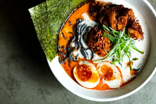 A bowl of noodle soup with nori, a halved egg, spring onion and fried meat