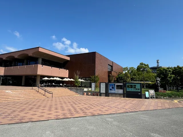 A red brick building with a paved plaza, steps and white parasols under a blue sky