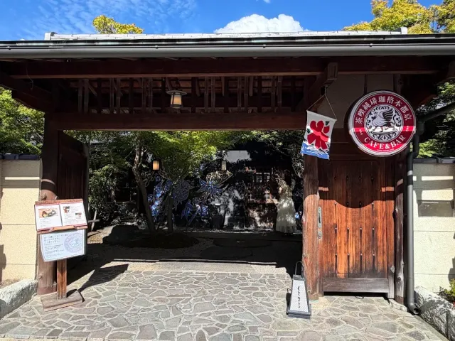 A traditional wooden gate with a tiled roof, a round red sign and a green garden behind it