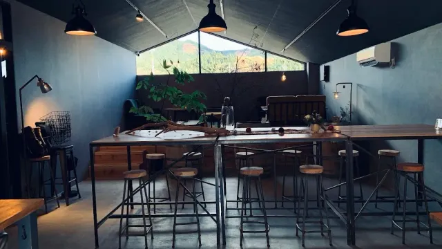 A space with high tables and stools, industrial lamps and a triangular window onto hills