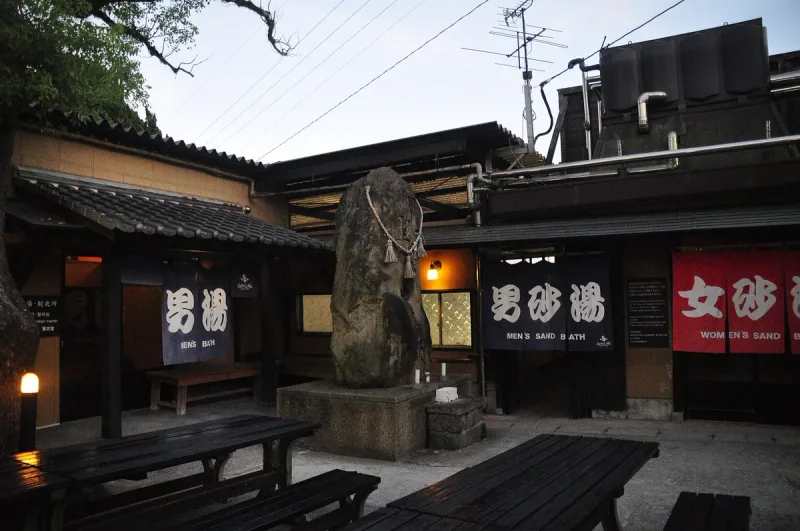 An onsen entrance with Japanese signage, a large stone and a wooden bench