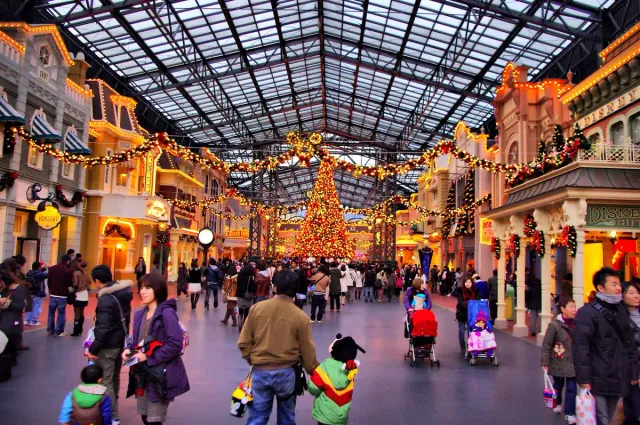 A covered, illuminated arcade with a decorated tree and crowds