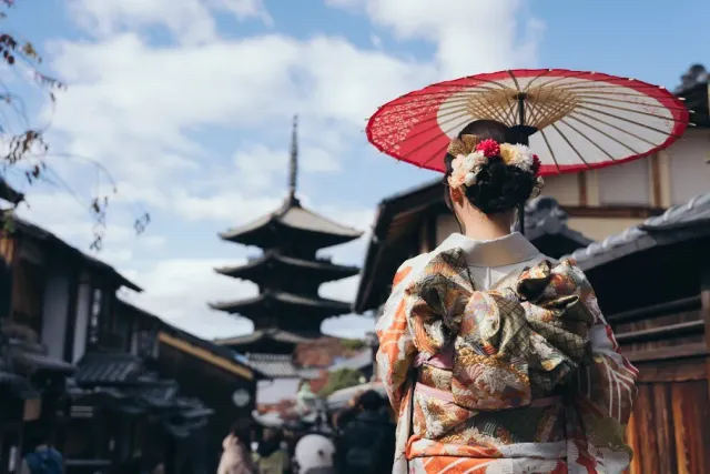 A woman in kimono seen from behind holding a red parasol, a five storey pagoda in the background