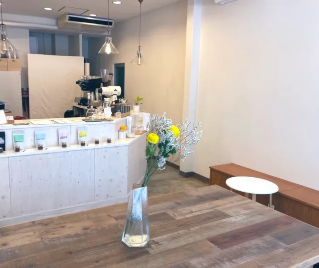 A white counter with an espresso machine, and in front a wooden table with a flower vase