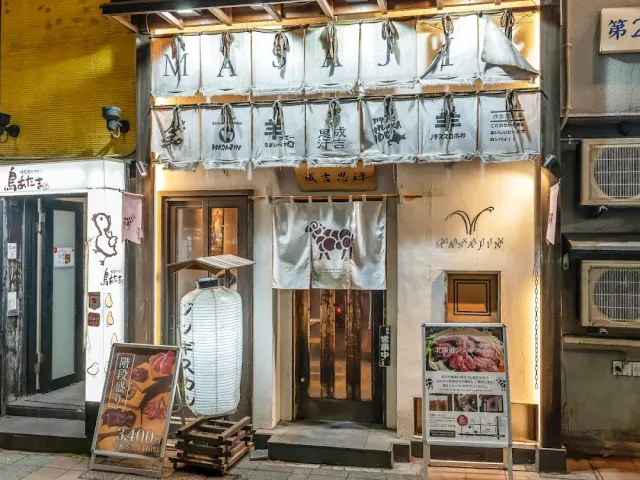 A frontage at night with hanging white banners, a curtain with a sheep figure, a paper lantern and menu boards