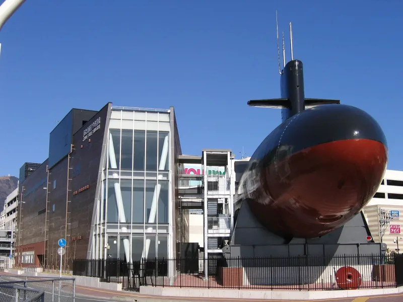 The black bow of a submarine displayed outside a glass clad museum building