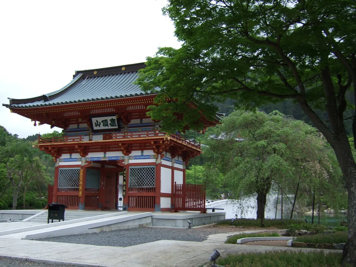 A red two-story temple gate at Katsuoji, surrounded by green trees in the mountains of Minoh