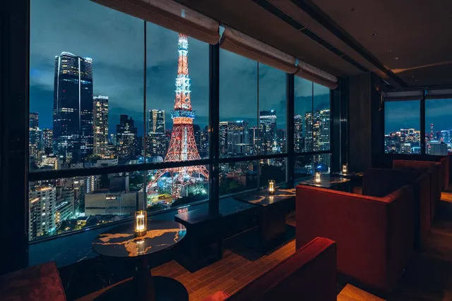 Red sofas facing huge windows with the illuminated Tokyo Tower behind them at night