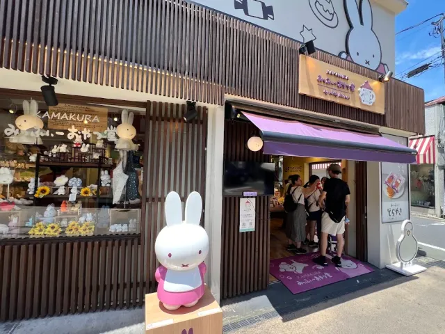 A shopfront on a narrow street with a large white rabbit statue and a queue of people at the entrance
