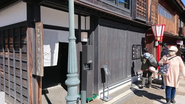 A street with dark wooden facades, a carved sign, a white cloth curtain and a hanging red lantern