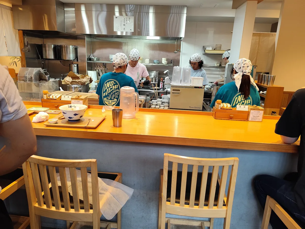 Open kitchen counter at Men-ya Inoichi ramen shop in Kyoto, staff wearing shirts printed with the Inoichi logo preparing noodles