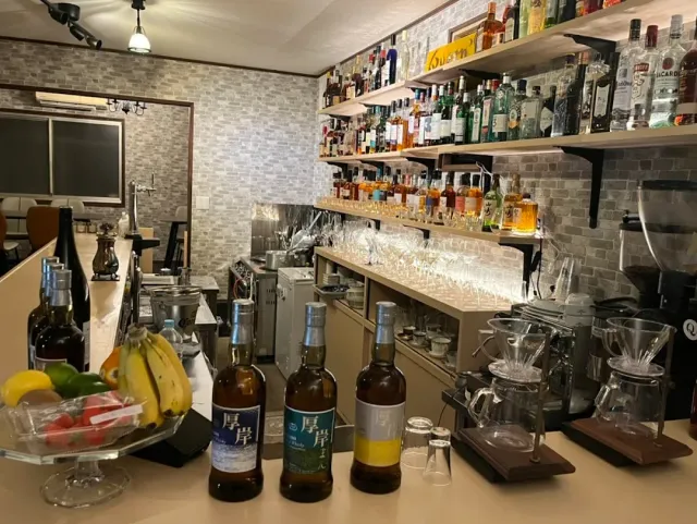 A counter with whisky bottles, a fruit bowl and shelves loaded with drinks behind