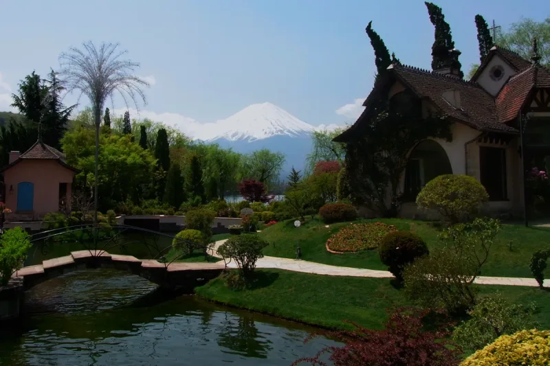 A landscaped garden with a pond and European style buildings, with snow capped Mount Fuji on the horizon