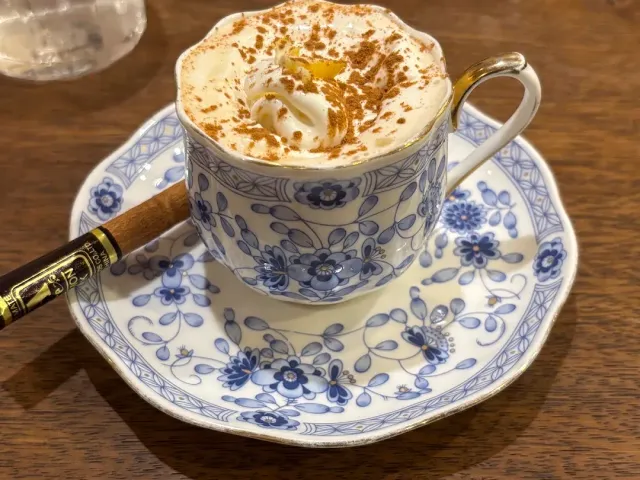 A blue and white floral cup with cream and cinnamon powder, on a matching saucer