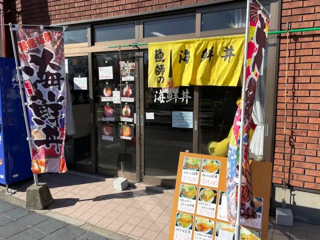 A frontage with a yellow curtain, street banners and a photo menu board beside a glass door