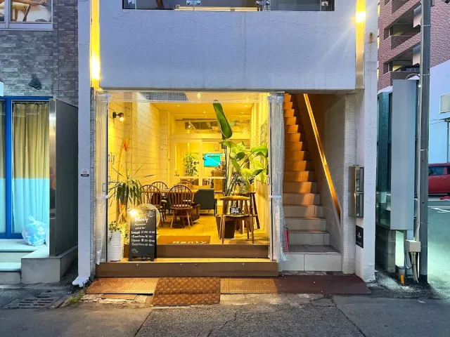 An open lit storefront in the evening with wooden chairs, potted plants and a chalkboard