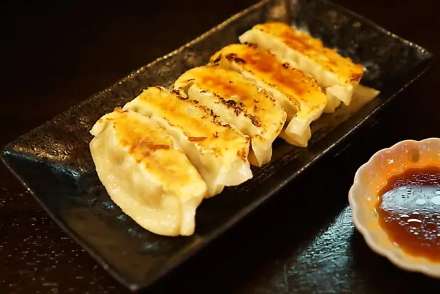 Fried dumplings on a dark rectangular plate beside a small bowl of sauce
