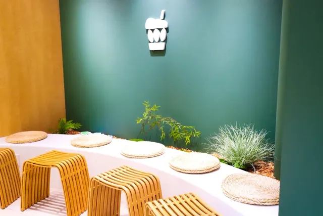 A green wall with a cup shaped sign, a curved white bench with mats and wooden stools