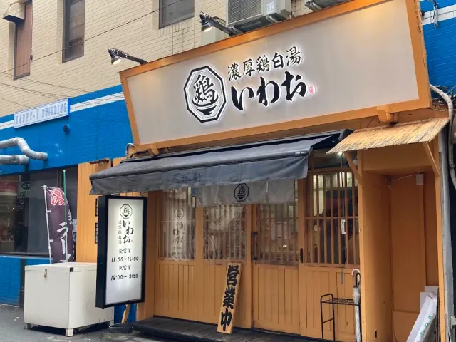 A frontage with a white sign and Japanese script, a grey awning, pale wooden doors and a standing sign