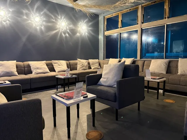 A lounge with grey sofas, pale cushions and low tables beside windows