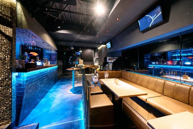 A bar with blue lighting, pale leather sofas and screens hanging on the wall