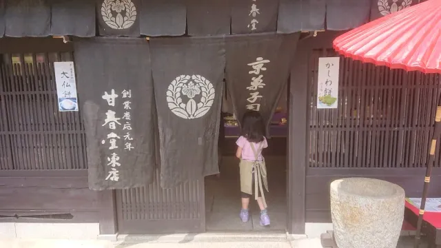 A girl stepping through the dark cloth curtain of an old wooden shop, beside a red parasol