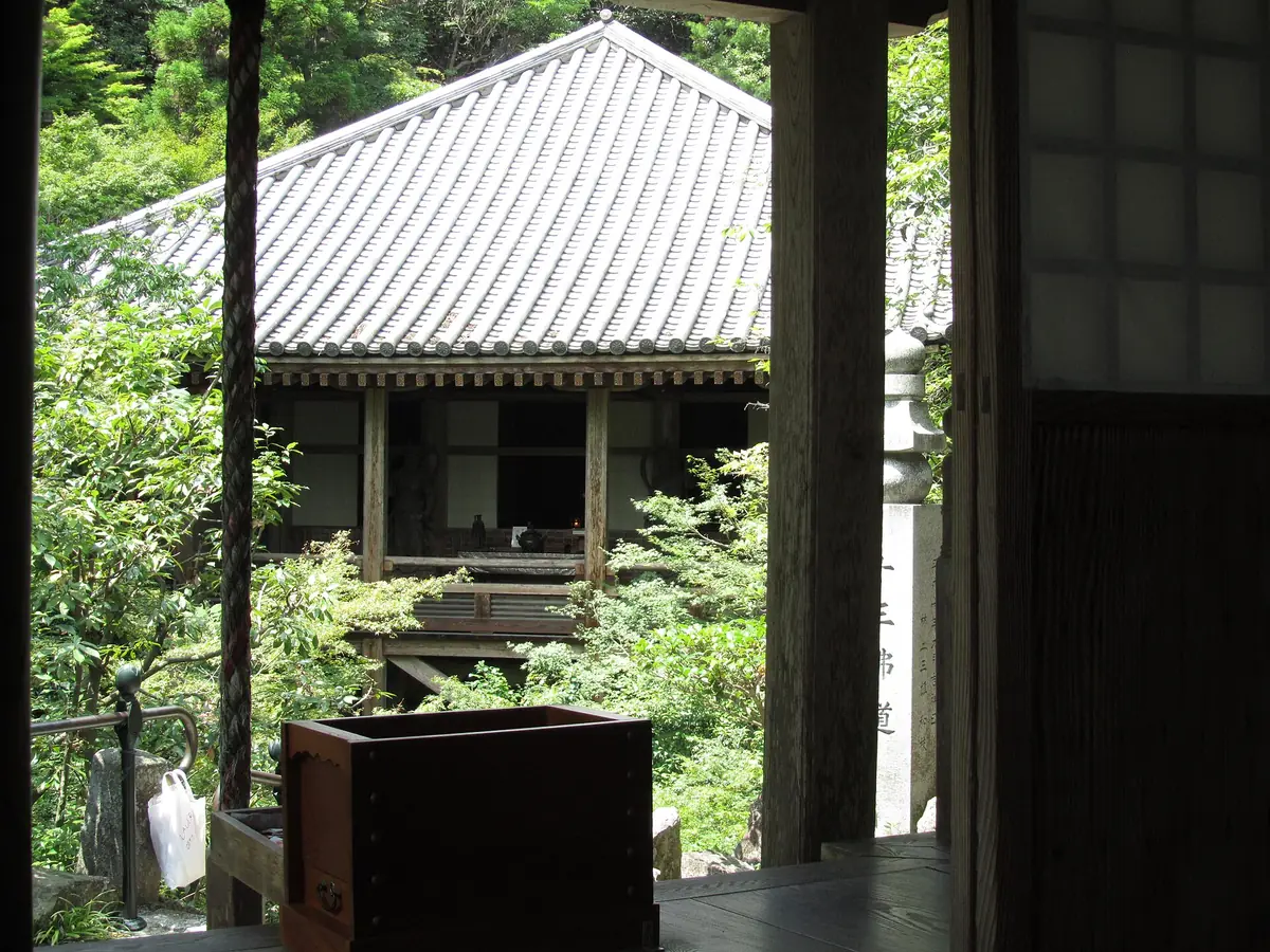 A wooden temple hall with a tiled roof among green trees