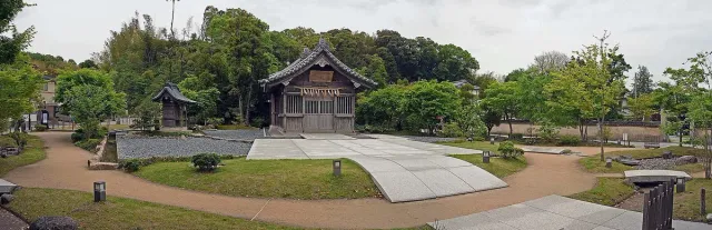 A wooden shrine hall with a wide paved courtyard and trees around